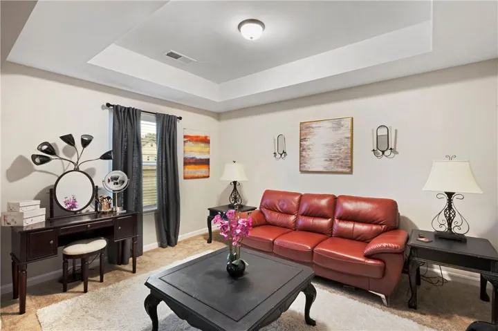 This inviting space in the primary suite features a tray ceiling, soft carpet, and warm natural light.
