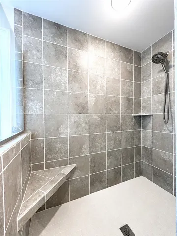 This spacious shower features tiled walls and a convenient corner bench.