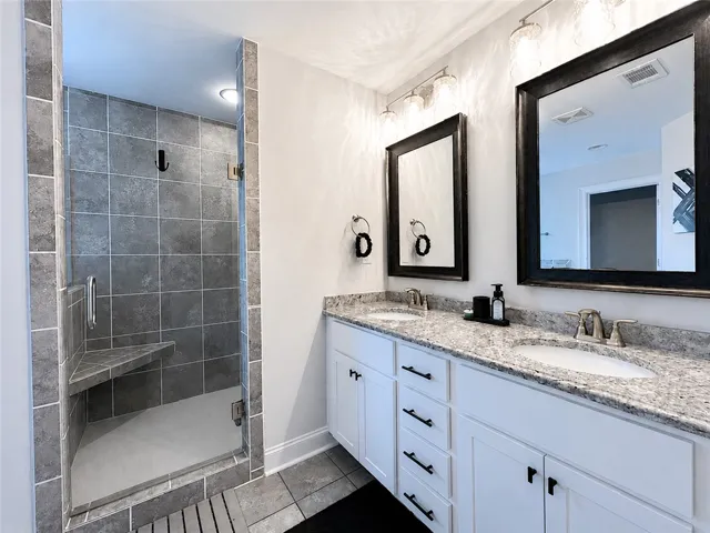 This primary bathroom features a double vanity and a glass-enclosed shower.