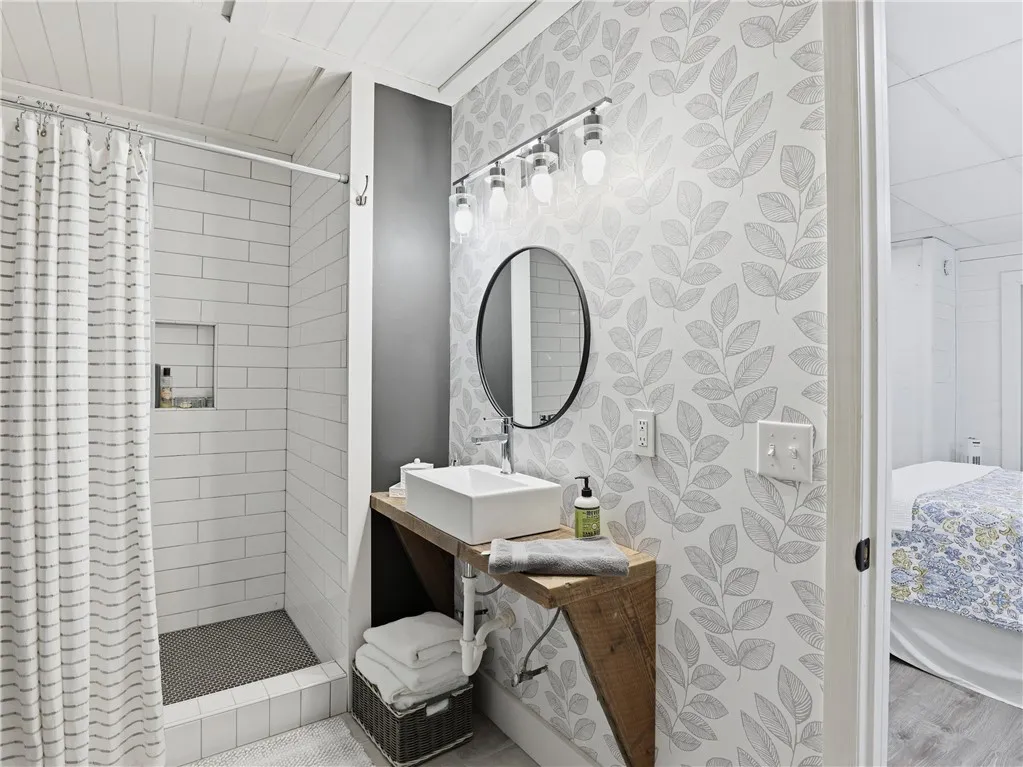 This functional bathroom features a shower with subway tile, a unique wooden vanity, and a stylish round mirror.