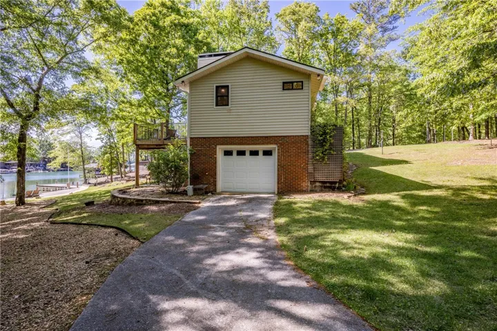This lakeside home features a garage and a balcony, nestled amidst lush trees and green lawn.