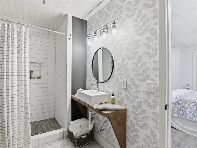 This functional bathroom features a shower with subway tile, a unique wooden vanity, and a stylish round mirror.