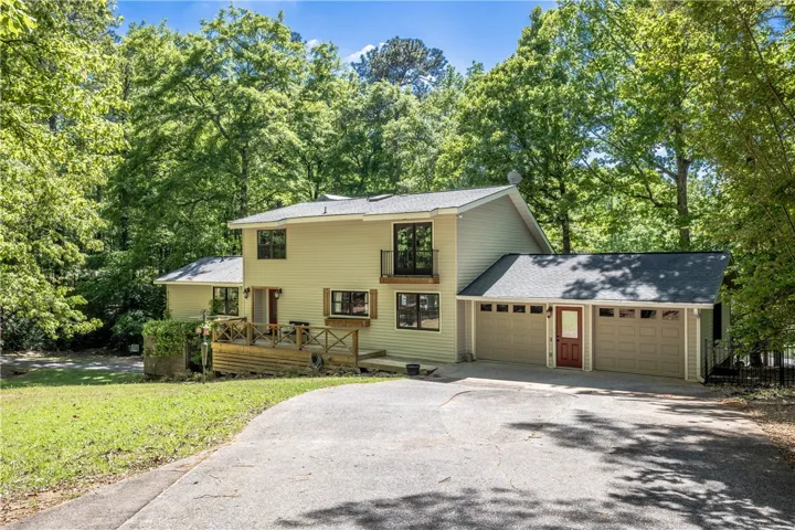 This secluded property features a large driveway, attached garage, and a charming wooden deck.