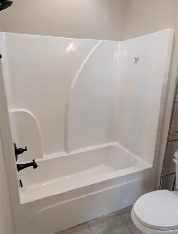 This bathroom features a sleek bathtub with a modern shower surround and tiled flooring.