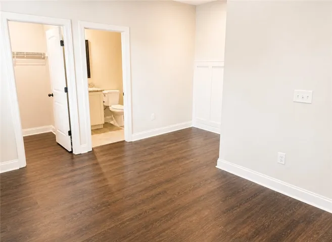 This bedroom features rich flooring, leading to an adjacent closet and an en suite bathroom.