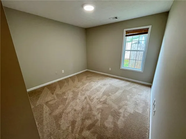 This cozy bedroom features plush carpet and a bright window, offering a serene personal retreat.