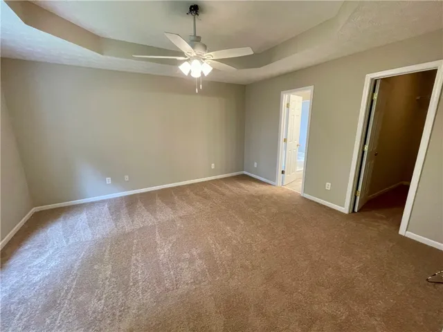 Relax in this comfortable primary bedroom, featuring a tray ceiling and soft carpet.
