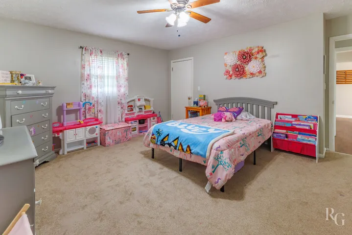 This cozy bedroom offers a comfortable retreat with soft carpet and a classic ceiling fan.