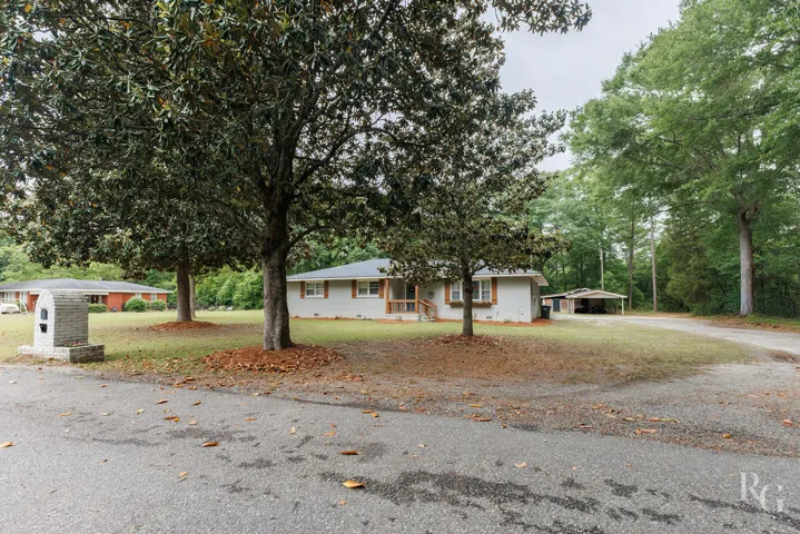 This inviting residence features a well-maintained exterior with mature trees and a functional carport.