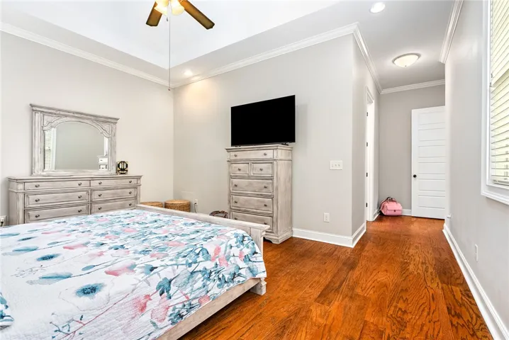 This spacious bedroom features elegant hardwood flooring and tray ceilings, creating a refined and inviting atmosphere.