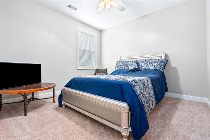 This inviting bedroom features soft carpeting, a bright window, and a ceiling fan for comfort.