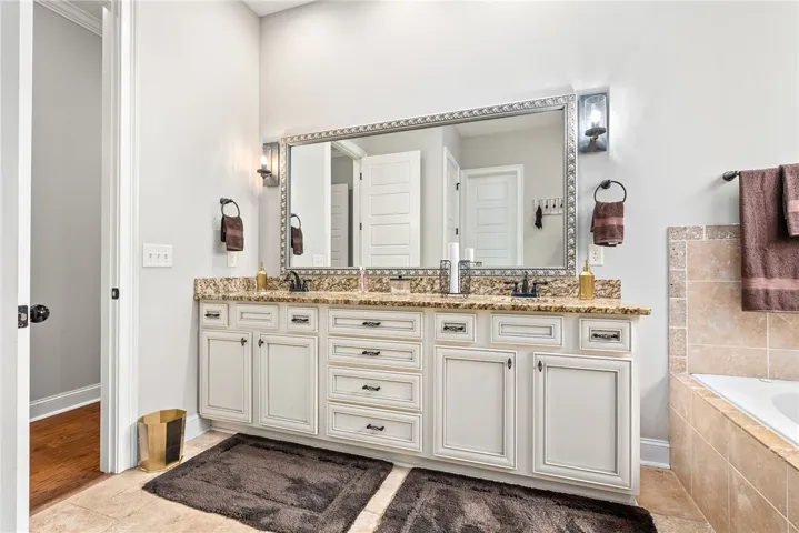 Elegant primary bathroom features a dual vanity with granite counters and a large mirror.