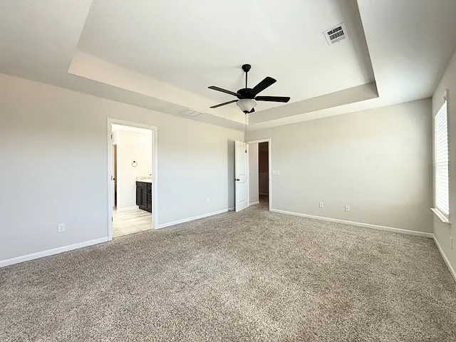 This spacious primary bedroom features soft carpet flooring, an elegant tray ceiling, and a private ensuite bathroom.