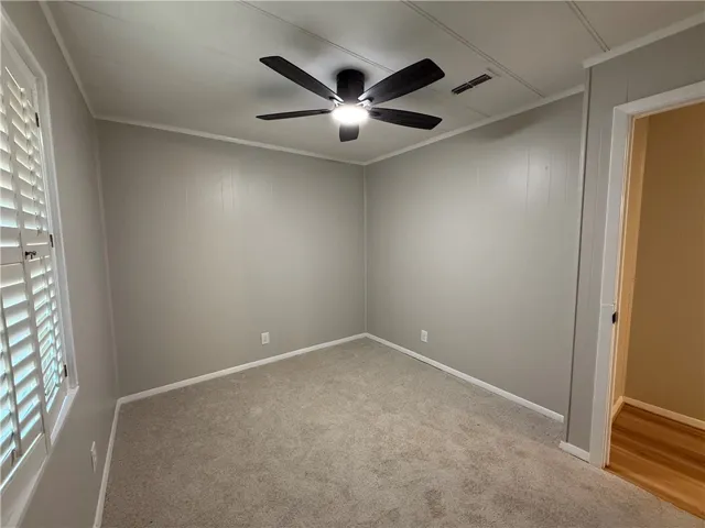 This cozy bedroom features carpeted floors, window shutters, and a ceiling fan.