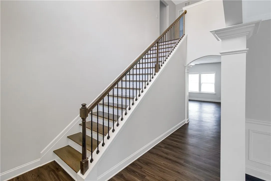 Elegant hardwood flooring leads the eye up a classic staircase with refined dark wood and wrought iron banisters.