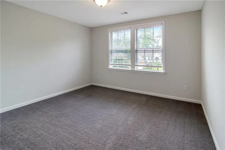 A well-lit bedroom features plush carpeting and broad windows.