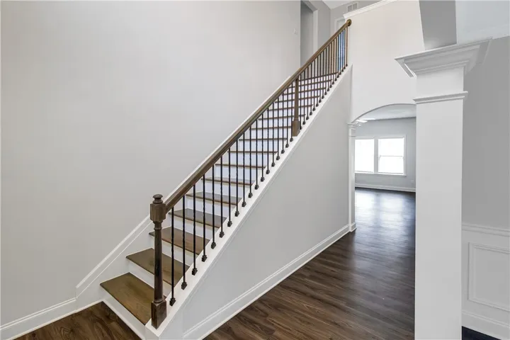 Elegant hardwood flooring leads the eye up a classic staircase with refined dark wood and wrought iron banisters.
