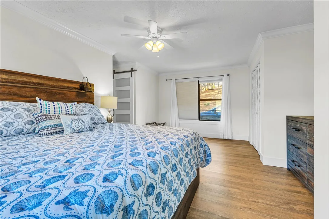 This bright and airy bedroom features crown molding, wood flooring, and a modern barn door.