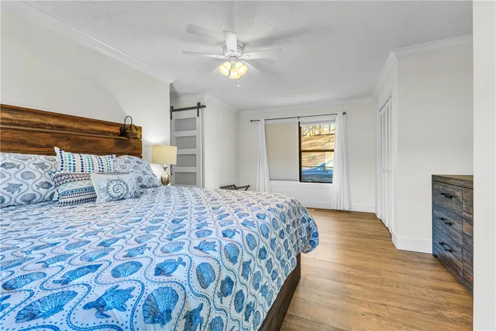 This bright and airy bedroom features crown molding, wood flooring, and a modern barn door.