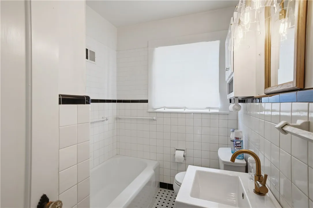 This bathroom features classic tile work, a clean tub, and a vanity with a contemporary faucet.
