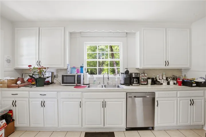 This bright kitchen features ample white cabinetry and a window overlooking lush greenery.