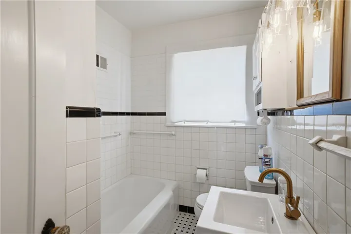 This bathroom features classic tile work, a clean tub, and a vanity with a contemporary faucet.