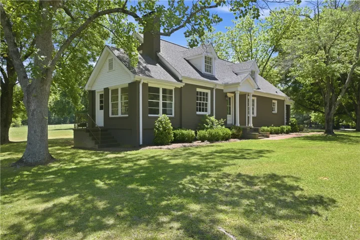 This charming residence offers a welcoming facade nestled amidst mature trees and a verdant lawn.