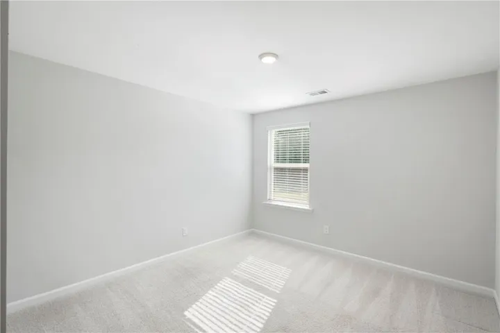 This bright bedroom features soft carpeting and a window with blinds, creating a comfortable and inviting space.