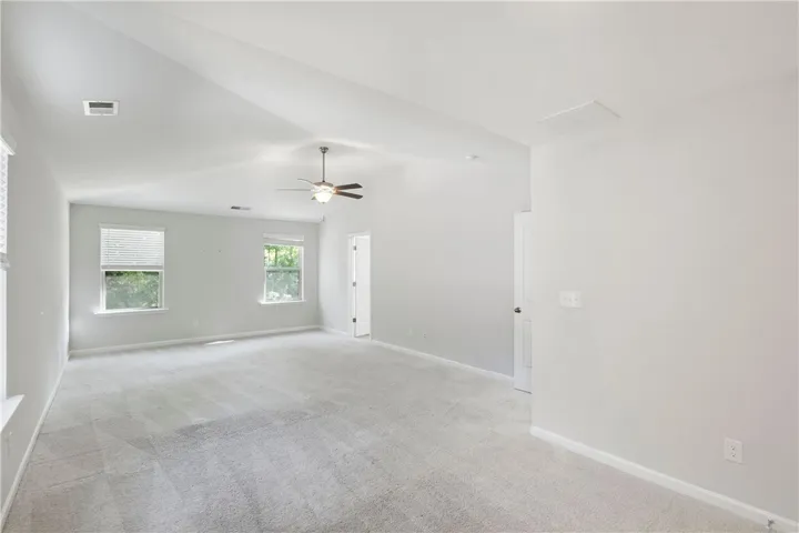 This spacious primary bedroom features soft carpeting, vaulted ceilings, and ample natural light from multiple windows.
