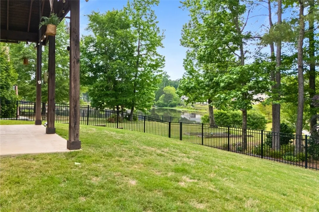 The lot go beyond the fence and trees to the sidewalk