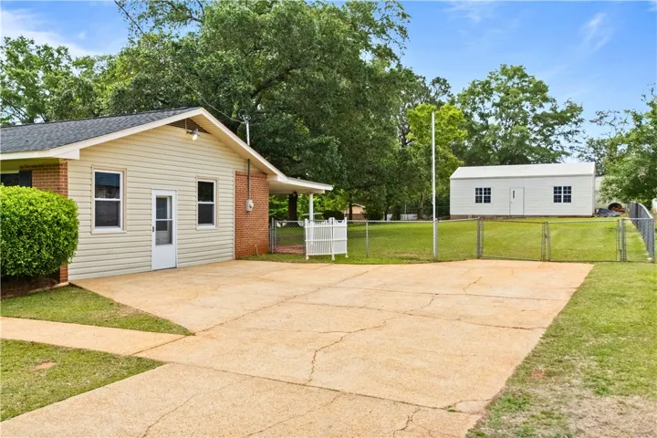 This property features a spacious driveway and a separate utility building, set against a backdrop of mature trees.