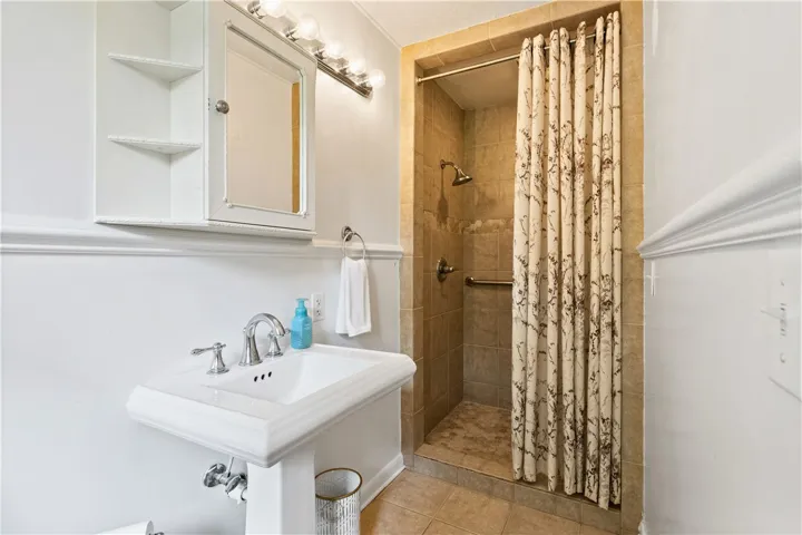 This bright bathroom features a classic pedestal sink and a tiled shower with grab bar.