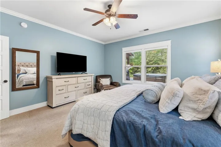 This restful bedroom features a ceiling fan, crown molding, and plush carpeting.