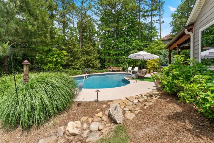 An inviting backyard oasis features a glistening pool, surrounded by lush foliage and a cozy patio.