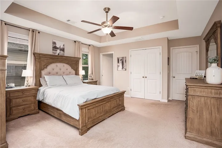 This inviting bedroom features soft carpeting, tray ceilings, and ample natural light, perfect for relaxation.