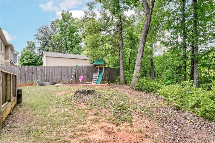 This spacious backyard offers privacy and room for recreation, featuring a wood fence and mature trees.