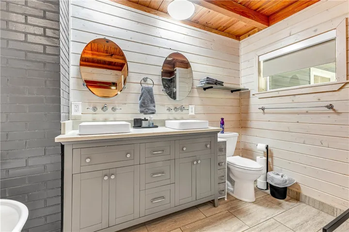This bathroom features a double vanity with elegant vessel sinks and a unique wooden plank and brick wall design.