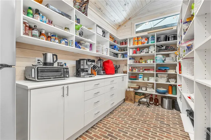 This spacious pantry features ample storage with shelving and a durable brick floor.