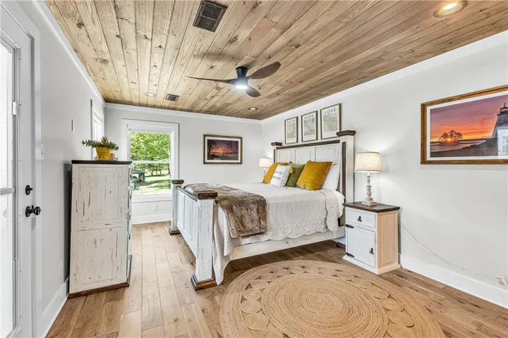 This airy bedroom features a rustic wood ceiling and durable hardwood flooring, creating a serene retreat.