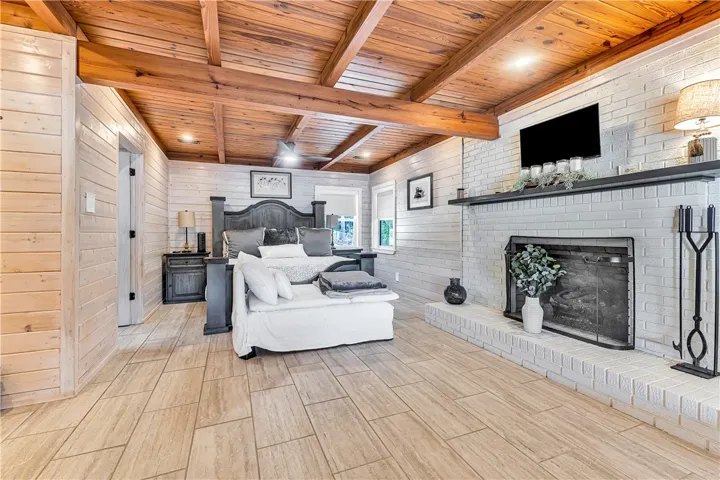 This spacious primary bedroom offers exposed wood beam ceilings and a cozy brick fireplace.