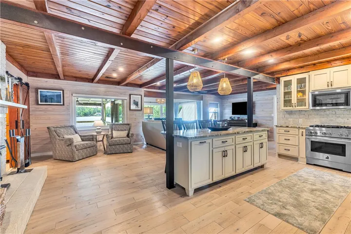 This inviting space features a kitchen island, a cozy living area, and wooden ceiling beams.
