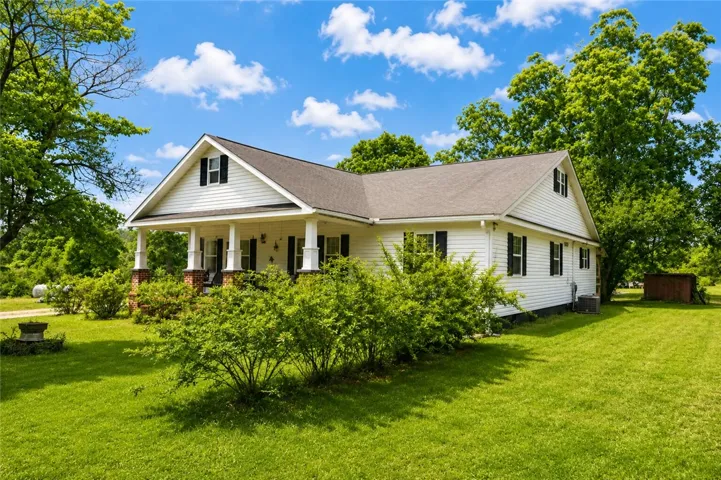This charming home features a welcoming porch, lush green lawn, and mature trees for serene outdoor living.