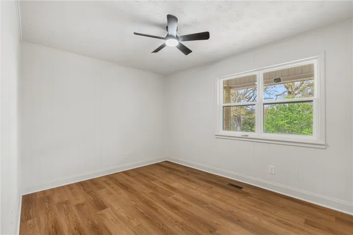 This bright room features beautiful flooring, a ceiling fan, and a serene view of lush greenery.
