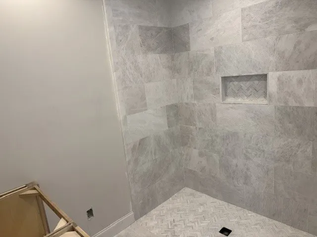 Elegantly tiled walk-in shower features sophisticated herringbone patterns and a built-in storage niche.