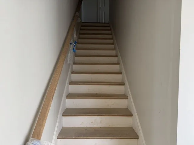 Natural wood treads and a matching handrail line this straight interior staircase.