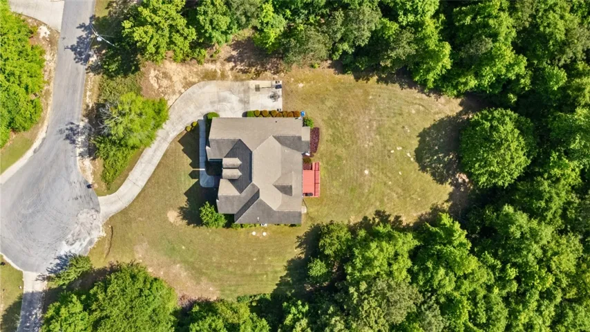 An aerial view showcases a residence nestled amidst lush green foliage and an expansive yard.