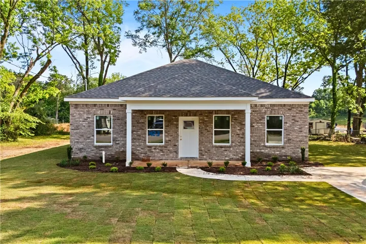 A charming single-story brick home awaits, nestled amidst lush greenery and mature trees.