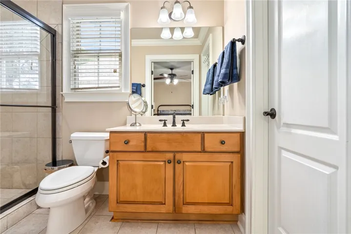 This bright bathroom features a vanity, window with blinds, and tiled shower area.