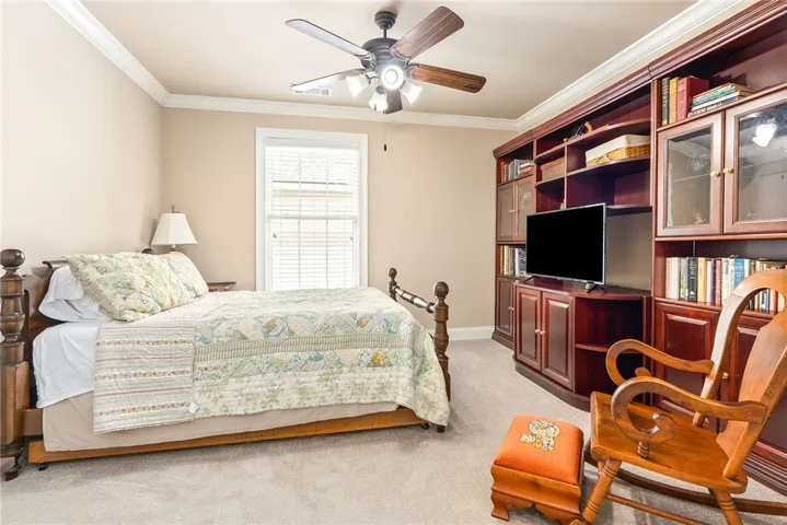 This cozy bedroom features a ceiling fan, a window, and ample built-in shelving.
