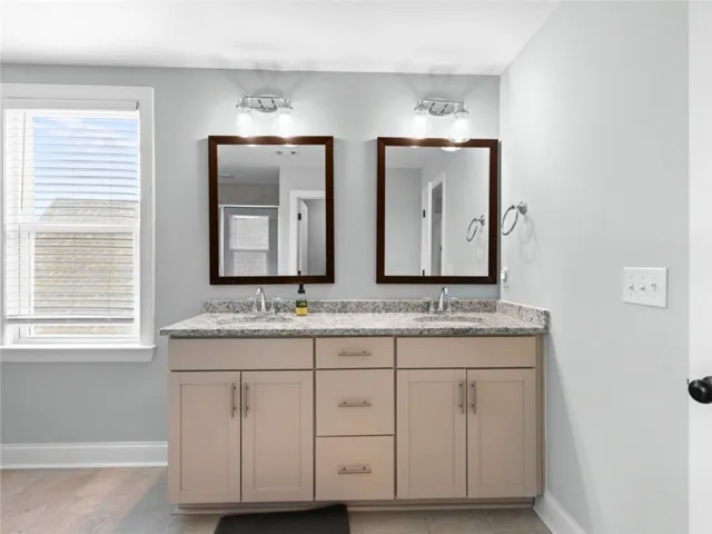 This bathroom features a double vanity with granite counters and a bright window.